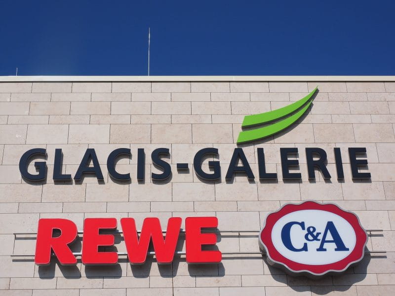 Auf einem Gebäude befinden zwei Schilder: REWE und C&A.