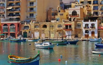 Eine typische Hafenstadt auf Malta: Im Vordergrund kleine Boote, im Hintergrund bunte Häuser.