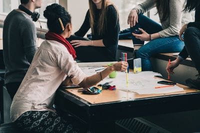 Fünf jüngere Erwachsene sitzen an einem Tisch und diskutieren.