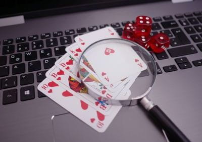 Pokerkarten, vier rote Würfel und eine Lupe liegen auf einer Laptoptastatur.